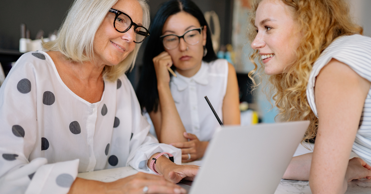 Three women sitting together, looking at a laptop screen and smiling.