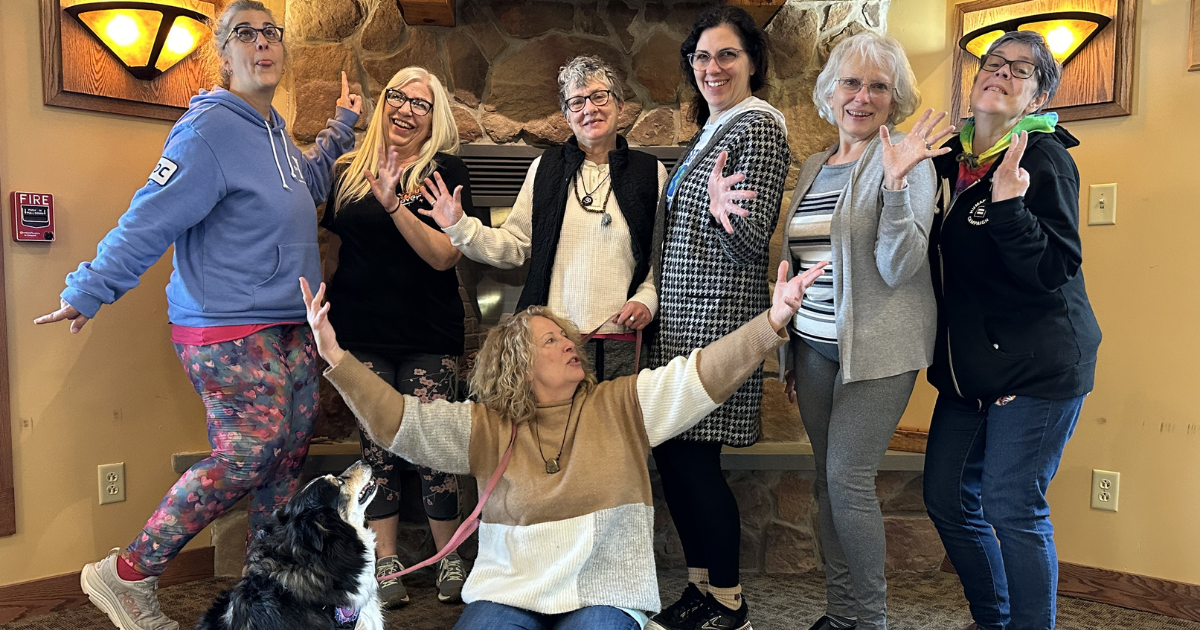 Group of women posing together with a dog in a room with warm lighting.