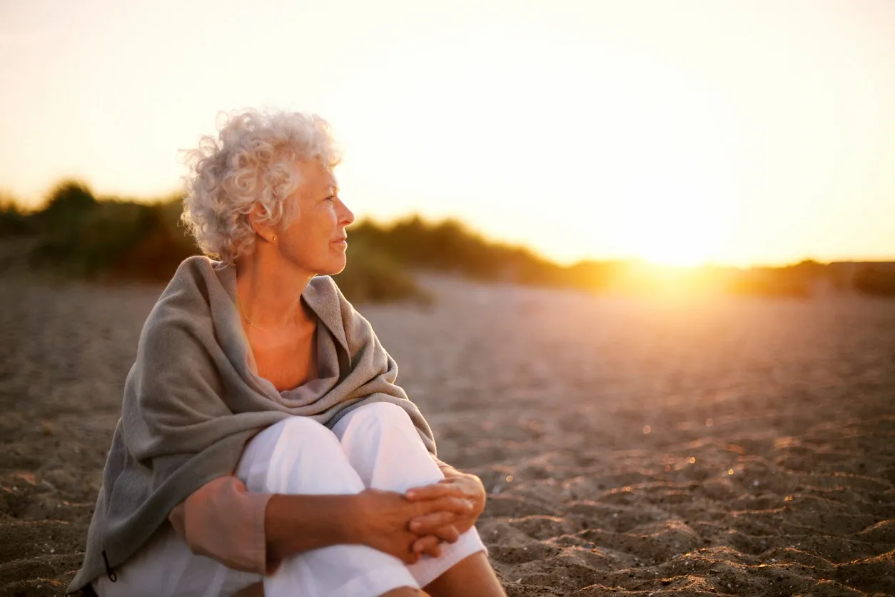Woman sitting on a beach at sunset, wrapped in a blanket.