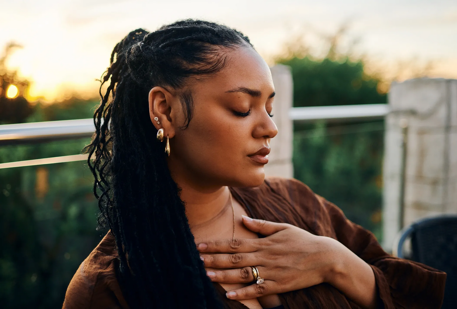 Woman with braided hair wearing a brown top, standing outdoors with blurred background
