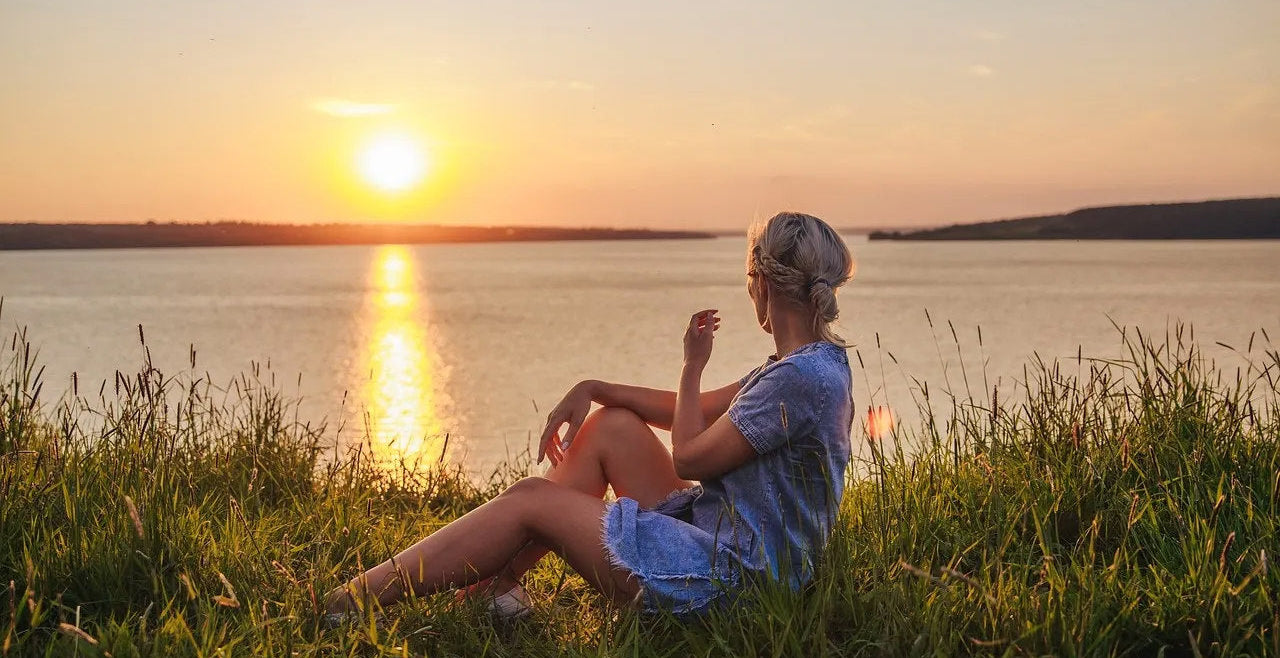 Person sitting by a lake at sunset