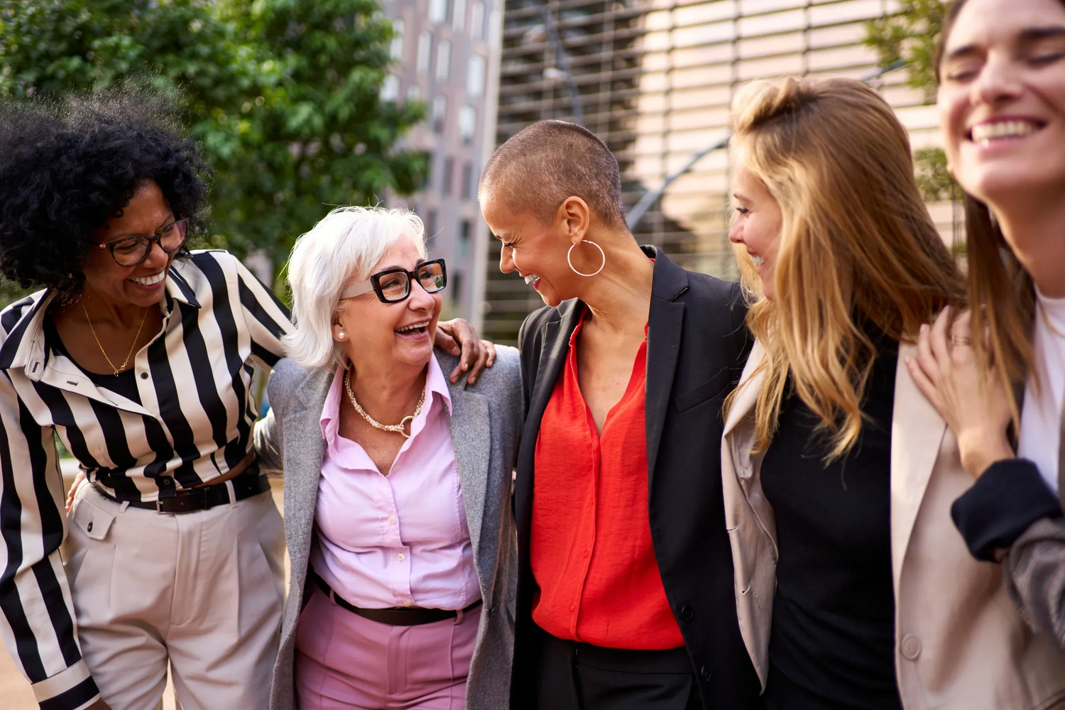 Group of women standing together outdoors, smiling and laughing.